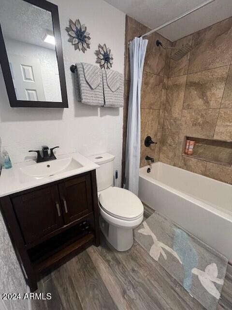 full bathroom with a textured ceiling, hardwood / wood-style floors, toilet, shower / bath combo with shower curtain, and vanity