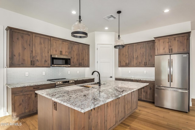 kitchen featuring light stone countertops, light hardwood / wood-style flooring, an island with sink, and appliances with stainless steel finishes