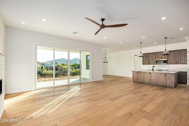 unfurnished living room featuring a fireplace, ceiling fan, sink, a mountain view, and light hardwood / wood-style floors