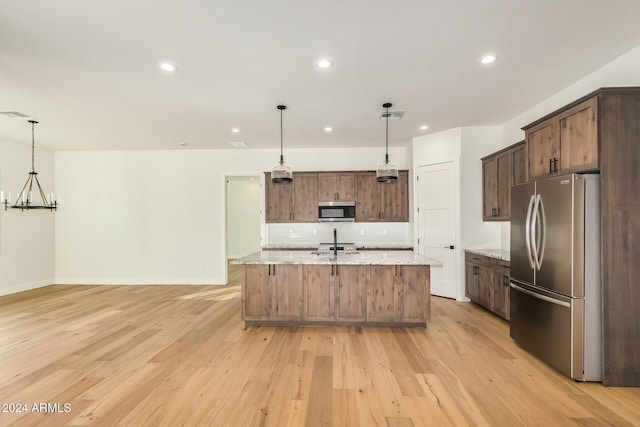 kitchen with light stone countertops, a center island with sink, stainless steel appliances, and light hardwood / wood-style floors