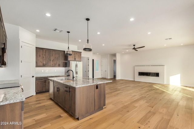 kitchen featuring light stone countertops, ceiling fan, hanging light fixtures, light hardwood / wood-style flooring, and a center island with sink