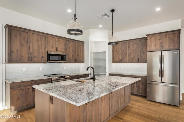 kitchen with a kitchen island with sink, sink, appliances with stainless steel finishes, and light hardwood / wood-style flooring