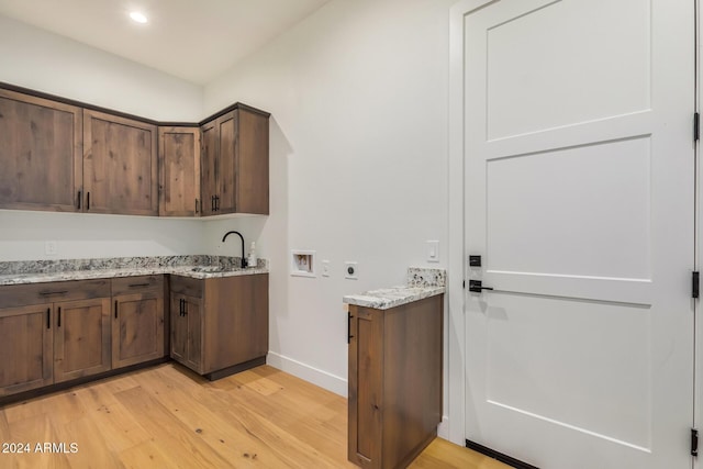 kitchen with dark brown cabinets, light stone countertops, and light hardwood / wood-style flooring