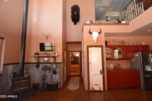 kitchen with a wood stove, glass insert cabinets, stainless steel refrigerator with ice dispenser, a towering ceiling, and wainscoting