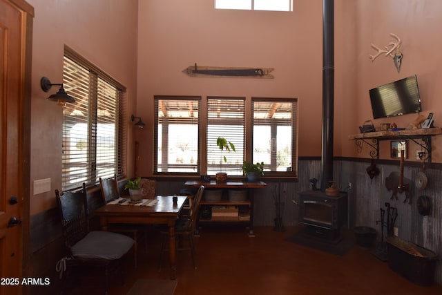 dining area with a wainscoted wall, a wood stove, and a high ceiling