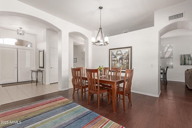 dining space with visible vents, wood finished floors, arched walkways, baseboards, and a chandelier