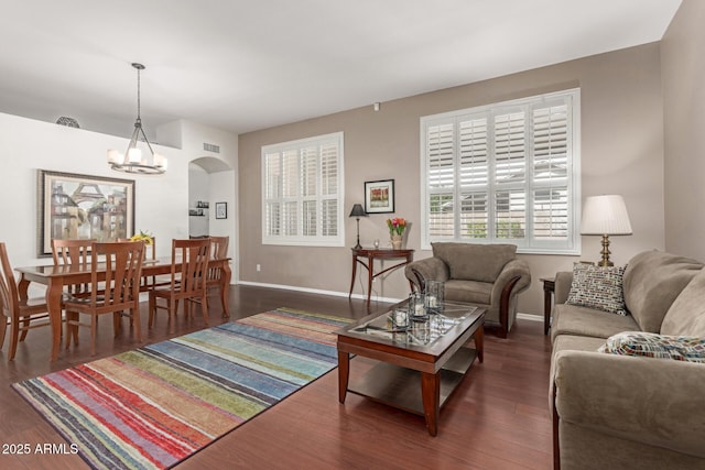 living area featuring visible vents, dark wood-style floors, arched walkways, an inviting chandelier, and baseboards