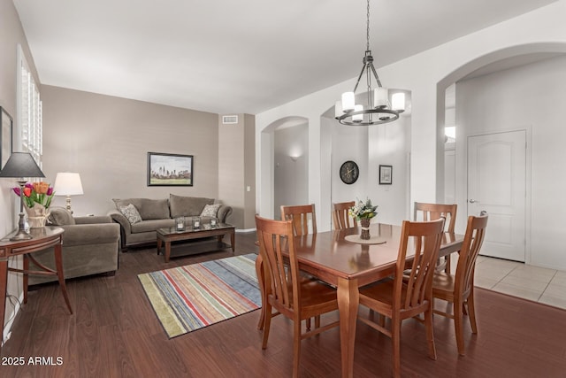 dining area with arched walkways, an inviting chandelier, and wood finished floors