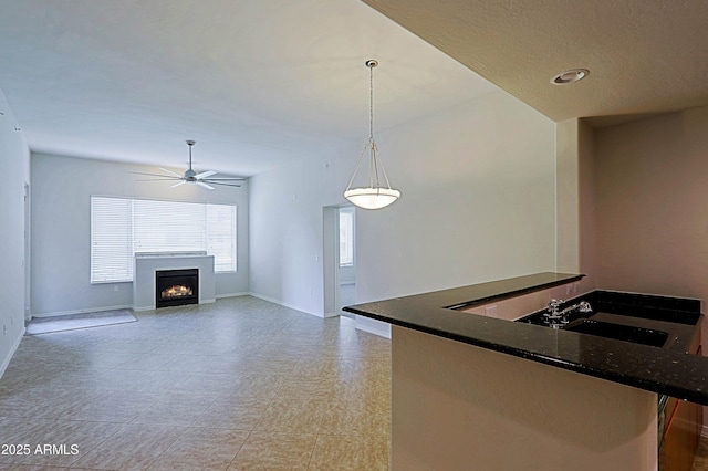 kitchen with ceiling fan, a warm lit fireplace, hanging light fixtures, and baseboards
