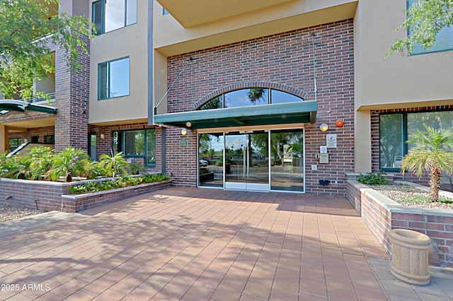 doorway to property featuring brick siding, stucco siding, and a patio