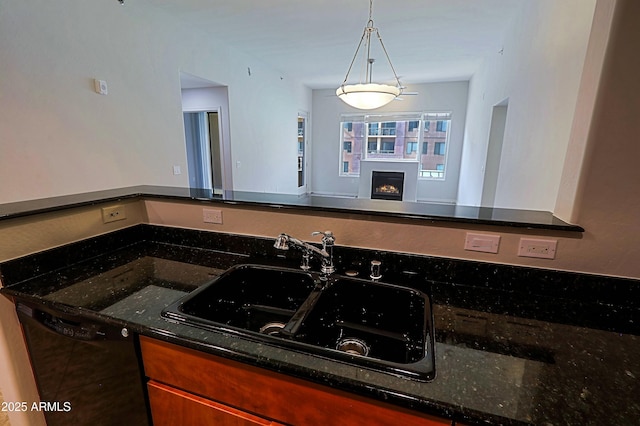 kitchen featuring a sink, black dishwasher, open floor plan, dark stone counters, and a lit fireplace