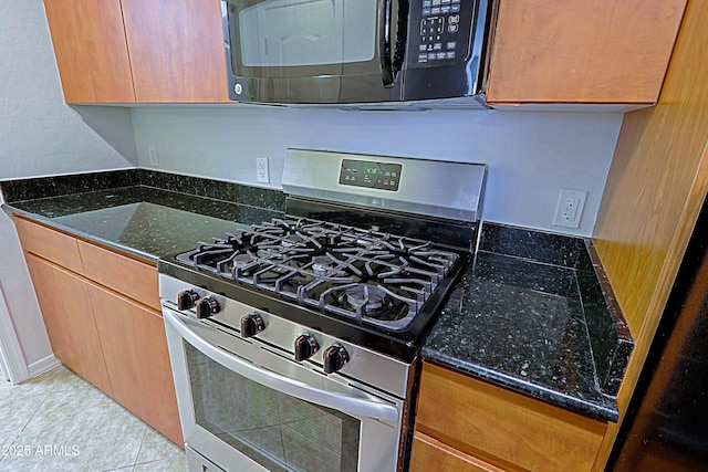 kitchen featuring stainless steel gas range oven, dark stone counters, and light tile patterned floors