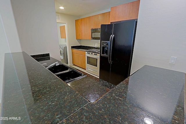 kitchen with black appliances, a sink, washer / dryer, dark countertops, and recessed lighting