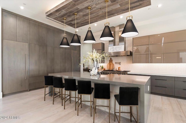 kitchen featuring light wood-type flooring, pendant lighting, wall chimney range hood, a kitchen breakfast bar, and backsplash