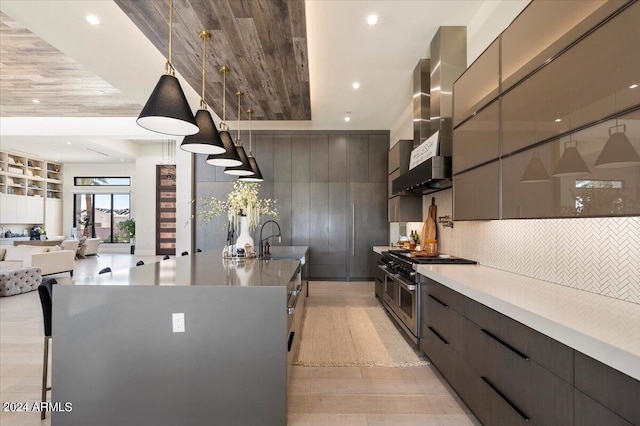 kitchen with range with two ovens, wall chimney range hood, pendant lighting, light hardwood / wood-style flooring, and a large island