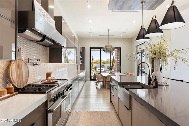 kitchen featuring wall chimney exhaust hood, range with two ovens, hanging light fixtures, light hardwood / wood-style flooring, and backsplash