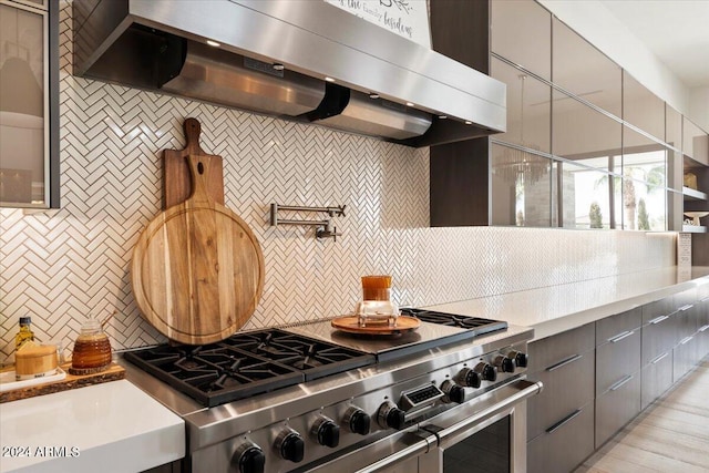 kitchen with light wood-type flooring, gray cabinetry, wall chimney range hood, high end stainless steel range, and backsplash