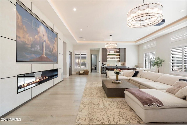 living room featuring a notable chandelier, a raised ceiling, and light hardwood / wood-style floors