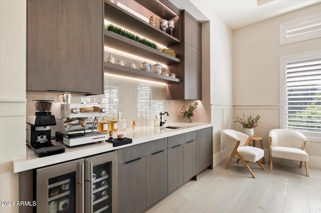 bar with light hardwood / wood-style floors, tasteful backsplash, dark brown cabinetry, wine cooler, and sink