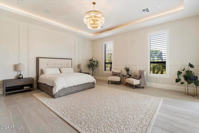 bedroom with an inviting chandelier, light wood-type flooring, and a tray ceiling