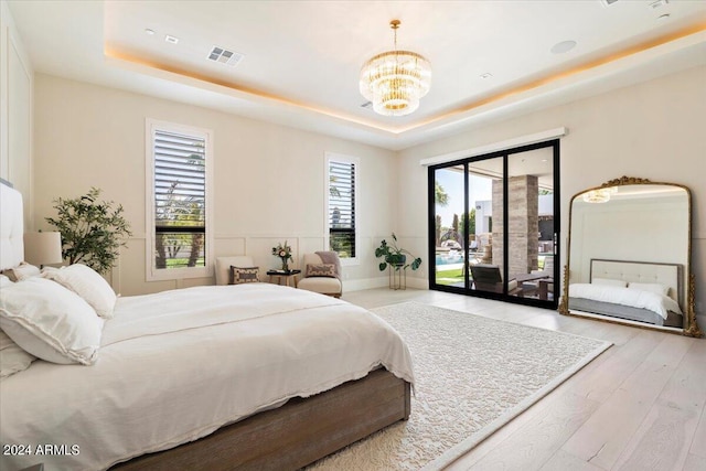 bedroom featuring access to outside, a raised ceiling, a chandelier, and light hardwood / wood-style floors