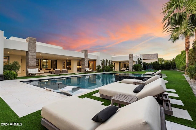 pool at dusk with outdoor lounge area, a lawn, and a patio area