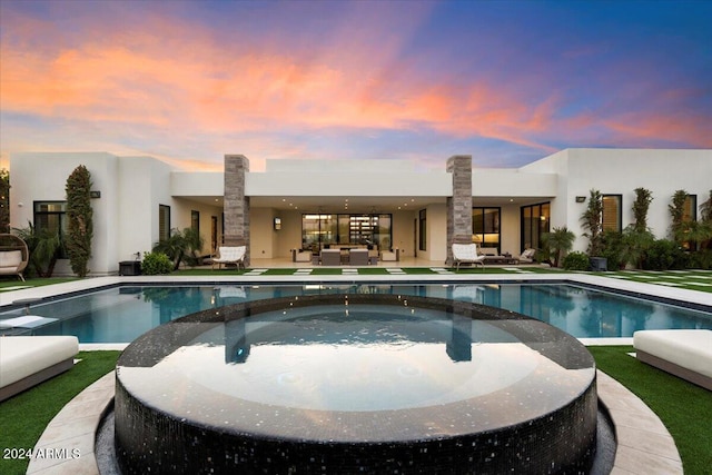 pool at dusk with an in ground hot tub and a patio