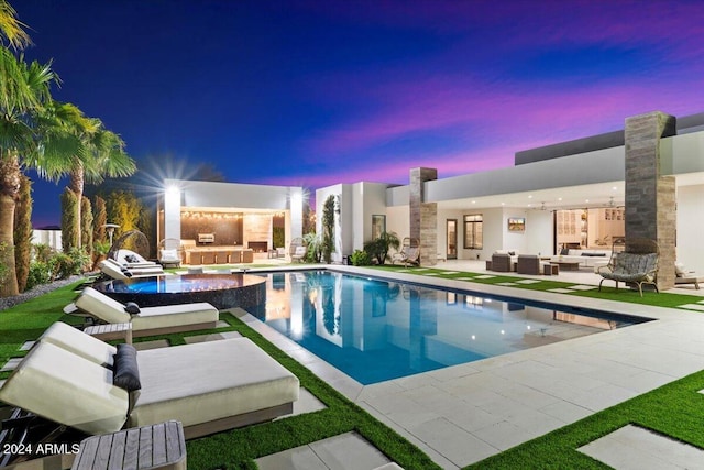 pool at dusk featuring an outdoor living space with a fireplace, a patio, and exterior kitchen