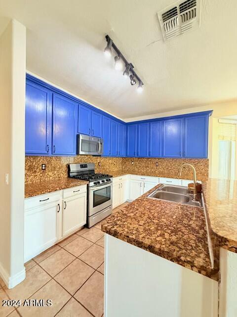 kitchen featuring blue cabinetry, sink, light tile patterned floors, stainless steel appliances, and decorative backsplash