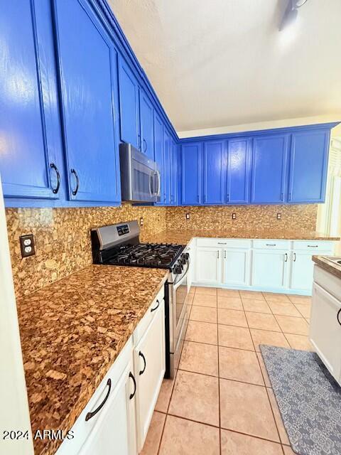 kitchen with appliances with stainless steel finishes, white cabinetry, decorative backsplash, light tile patterned floors, and blue cabinetry