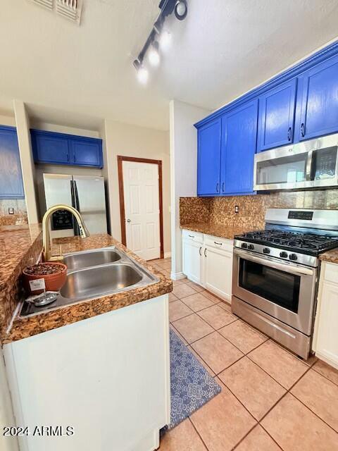 kitchen featuring blue cabinets, sink, tasteful backsplash, light tile patterned floors, and stainless steel appliances