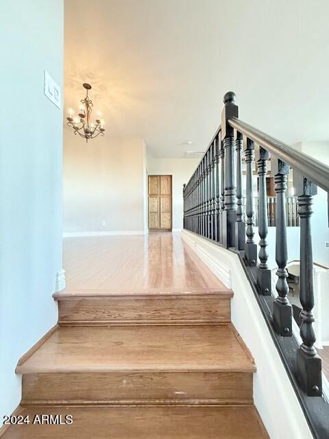 stairway with wood-type flooring and a notable chandelier