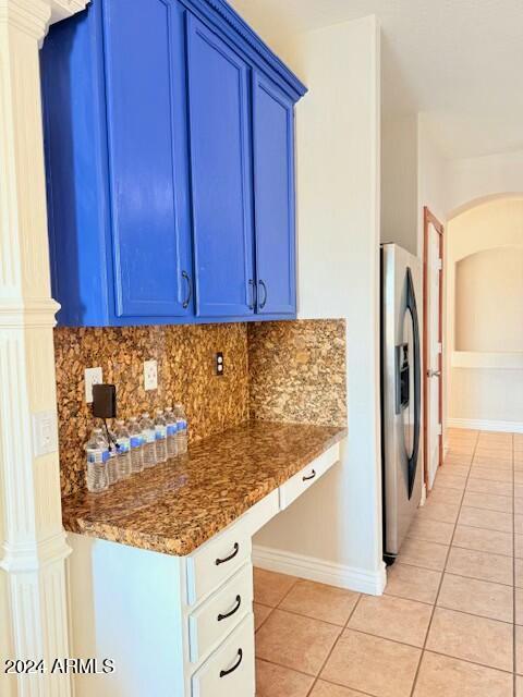 kitchen featuring stainless steel fridge, dark stone countertops, backsplash, blue cabinets, and light tile patterned flooring