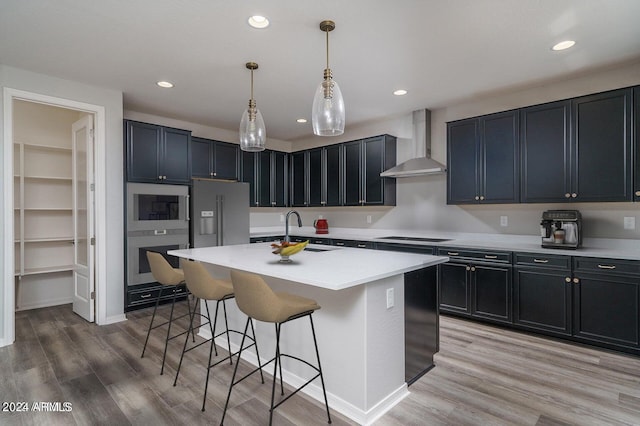 kitchen with a kitchen island with sink, hanging light fixtures, wall chimney exhaust hood, light hardwood / wood-style flooring, and high quality fridge