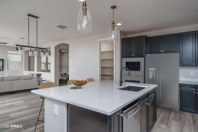 kitchen featuring light wood-type flooring, sink, stainless steel appliances, and an island with sink