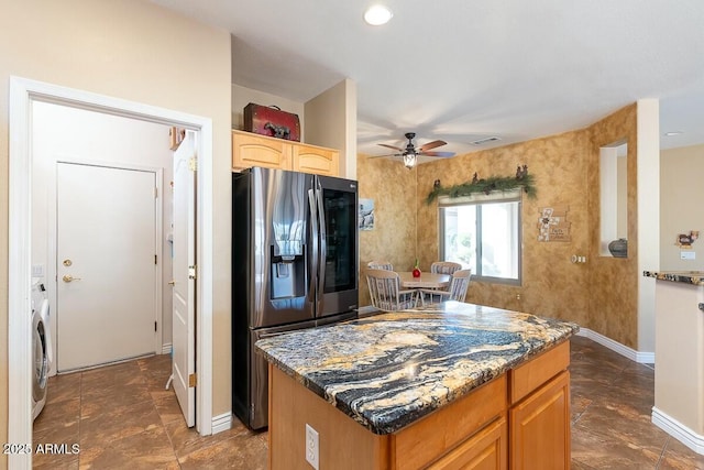 kitchen featuring stainless steel fridge, ceiling fan, washer / dryer, dark stone counters, and a center island