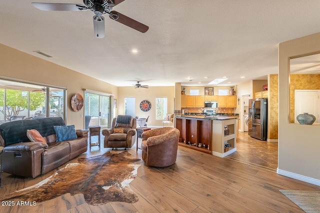 living room with light hardwood / wood-style floors, a textured ceiling, and ceiling fan