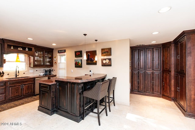 kitchen featuring dark brown cabinetry, hanging light fixtures, a breakfast bar area, and sink