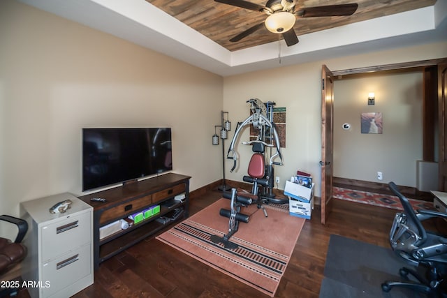 workout area featuring dark wood-style floors, a tray ceiling, baseboards, and a ceiling fan