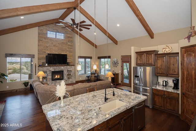 kitchen with stainless steel appliances, a sink, open floor plan, a large island, and light stone countertops