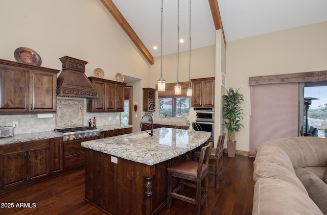 kitchen featuring decorative light fixtures, a sink, appliances with stainless steel finishes, tasteful backsplash, and a center island with sink