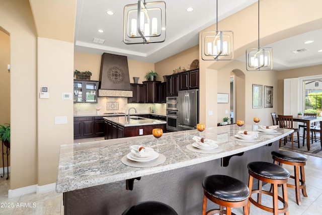 12904 W Dale Ln, Peoria, AZ 85383 - kitchen with stainless steel appliances, custom range hood, a large island, a raised ceiling, and arched walkways