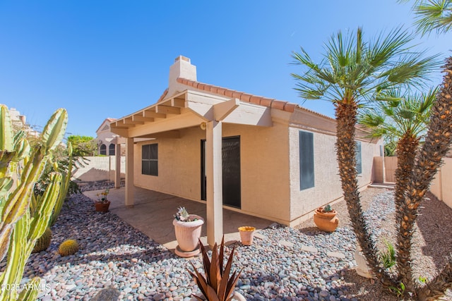 rear view of property with a patio, fence, a tiled roof, stucco siding, and a chimney