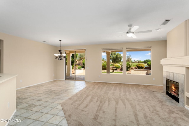 unfurnished living room with ceiling fan with notable chandelier, light carpet, and a tiled fireplace