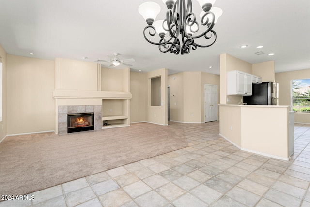 unfurnished living room with ceiling fan with notable chandelier, light colored carpet, and a fireplace