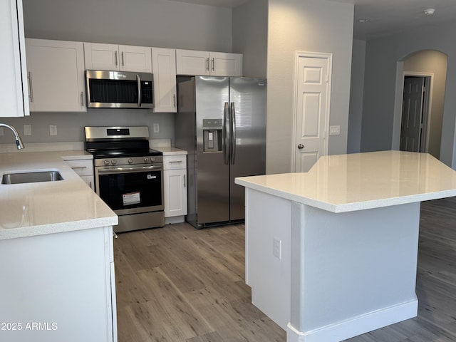 9224 W Raymond St, Tolleson, AZ 85353 - kitchen featuring appliances with stainless steel finishes, arched walkways, light wood finished floors, white cabinets, and a kitchen island