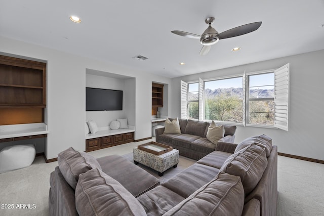 living room featuring built in desk, light colored carpet, and ceiling fan