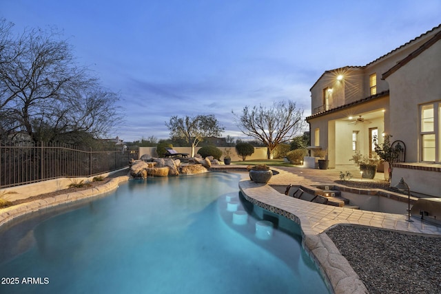 pool at dusk featuring ceiling fan and a patio area