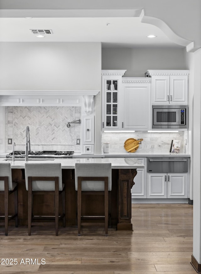 kitchen with a kitchen breakfast bar, dark hardwood / wood-style floors, stainless steel microwave, white cabinets, and a center island with sink