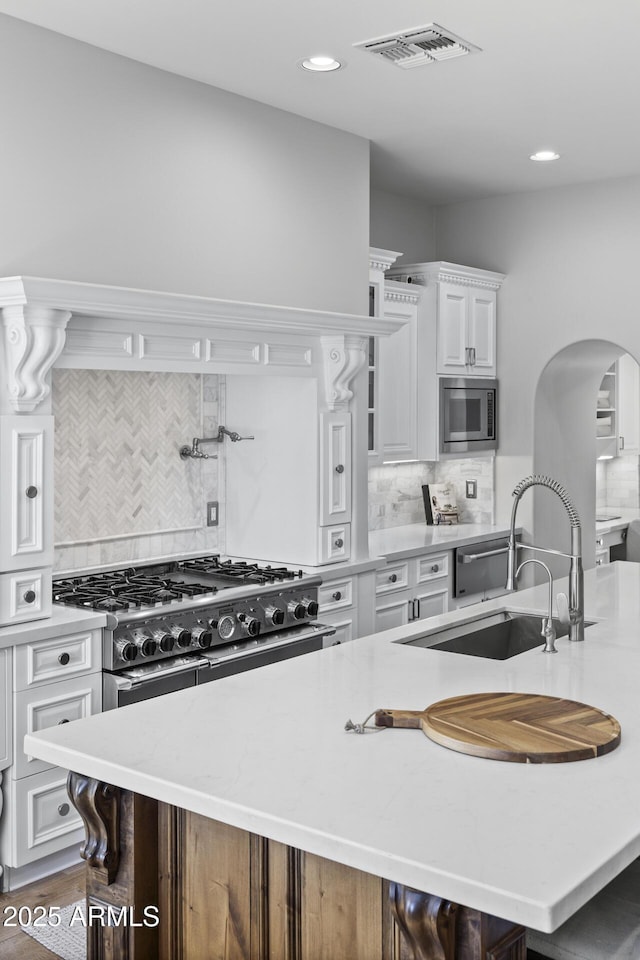 kitchen with stainless steel appliances, an island with sink, sink, and white cabinetry